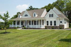 cream custom home with vinyl siding, stone veneer, large front porch, and attached garage