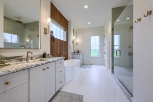 bathroom with split double vanities with soaking tub and wood accent wall with window between them and a walk-shower with a glass door on the opposite wall