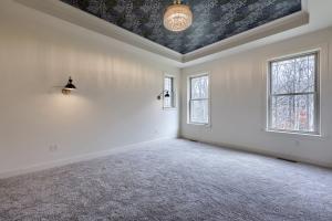 carpeted bedroom with 3 windows, wall sconces, and tray ceiling with dark patterned wallpaper
