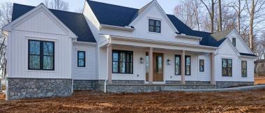 angled exterior view of white modern farmhouse custom home, with slate roof, covered front porch, and stone siding accent