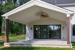 exterior view of covered patio with ceiling fan and large black frame sliding glass doors leading inside